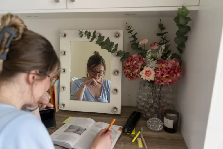 Student pluggar i studentlägenhet i Karlstad vid skrivbord med spegel och blommor.